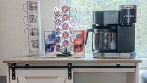 Una encimera de cocina con una cafetera, una taza de café, un tarro de leche y un azucarero.