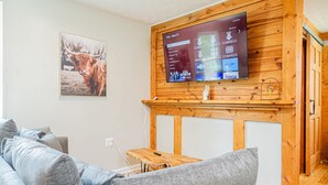 Una sala de estar con un televisor montado, un mueble bajo de madera, un sofá y un cuadro enmarcado en la pared.
