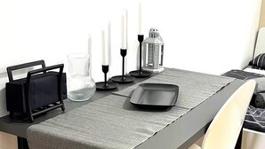 Een eettafel met een grijze tafelkleed, een zwart dienblad en witte kaarsen.