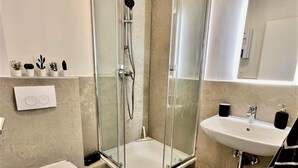 Een moderne badkamer met een douche met glazen wand, een wit toilet, een wastafel met spiegel en vloertegels met een patroon.