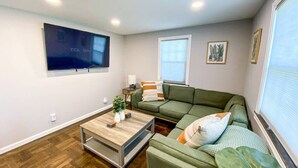 Una sala de estar moderna con un sofá seccional verde, una mesa de centro de madera y un televisor de pantalla plana montado en la pared.
