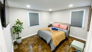 Un dormitorio con cama, una planta en maceta, un banco y dos ventanas con persianas.