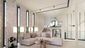 A spacious living room with a large sectional sofa, a round coffee table, and a stone accent wall. - Pnoe Seafront Experience | Villa Alas (Kolymvari)