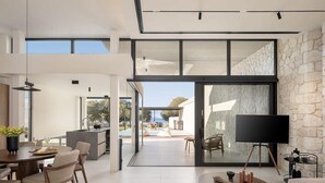 A modern interior with a dining area, kitchen, and a large sliding glass door leading to an outdoor space. - Pnoe Seafront Experience | Villa Alas (Kolymvari)