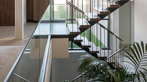 A modern interior with a glass railing, a staircase with metal railings, and a view of greenery outside. - Pnoe Seafront Experience | Villa Etheras (Kolymvari)