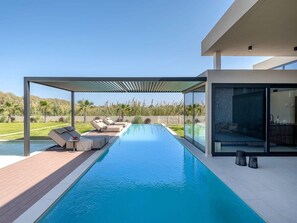Ein moderner Poolbereich mit freiem Blick auf das Schwimmbecken, Liegestühle und eine gläserne Struktur.