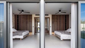 A modern bedroom with two beds, a ceiling fan, and a sliding glass door leading to an outdoor area. - Pnoe Seafront Experience | Villa Etheras (Kolymvari)