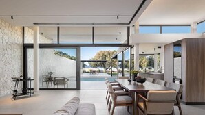 A spacious modern living area with a large dining table, comfortable seating, and a view of the outdoors. - Pnoe Seafront Experience | Villa Etheras (Kolymvari)