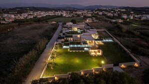 Un hotel moderno con piscina centrale, circondato da edifici ben illuminati e vista su una cittadina in lontananza.