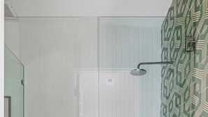 Une douche fermée par des parois de verre, avec un sol carrelé de blanc et un mur orné d’un motif vert.