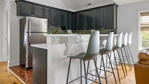 A modern kitchen with dark cabinets, a stainless steel refrigerator, and a bar area with stools. - Stylish Getaway in Downtown Charleston (Charleston)