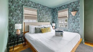 A bedroom with a bed, two windows with blinds, a ceiling fan, and a wall with a floral wallpaper pattern. - Stylish Getaway in Downtown Charleston (Charleston)