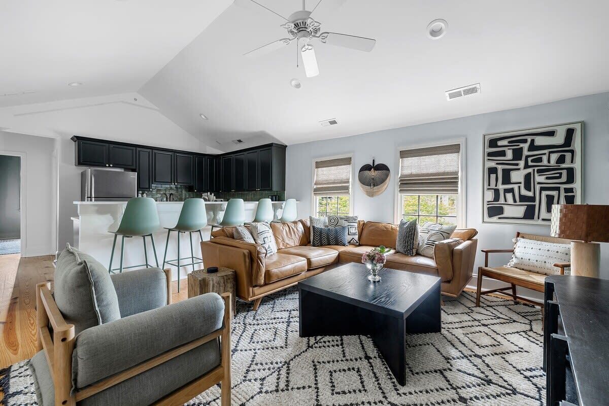 A modern living room with a sectional sofa, a coffee table, and a dining area with a kitchen in the background.