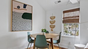 Un coin repas avec une table ronde, quatre chaises, une plante en pot et un grand tableau abstrait accroché au mur.