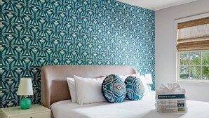 Un lit bien fait, agrémenté d’oreillers à motifs, une table de chevet avec une lampe et une brochure de bienvenue posée sur le lit.