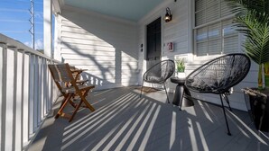 Une véranda couverte avec une table en bois et deux chaises, une plante en pot et une fenêtre avec des volets.