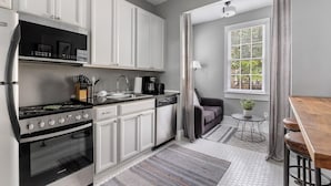 Een moderne keuken met witte kasten, een fornuis en een vaatwasser. Er is een eethoek met een houten tafel en barstoelen.
