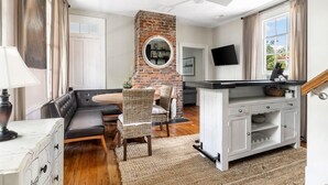Una sala de estar moderna con chimenea de ladrillo, comedor y cocina con un armario blanco y un televisor de pantalla plana.