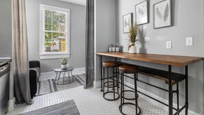 Una cocina moderna con un taburete de bar de madera, una ventana con cortinas e impresiones botánicas enmarcadas en la pared.