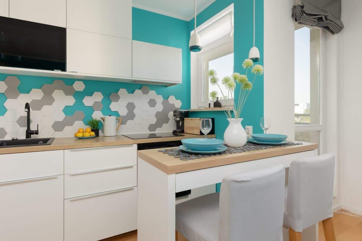 A modern kitchen with white cabinets, a teal backsplash, and a dining area with a wooden table and chairs.
