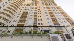 Un immeuble résidentiel de grande hauteur doté de nombreux balcons, de climatiseurs et d’une entrée sécurisée par un portail.