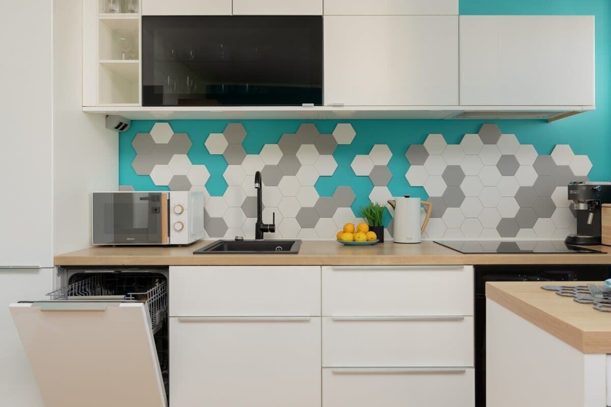 A modern kitchen with white cabinets, a black microwave, and a teal backsplash with hexagonal tiles.
