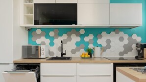 Une cuisine moderne avec des meubles blancs, un micro-ondes noir et un pare-feu turquoise orné de carreaux hexagonaux.