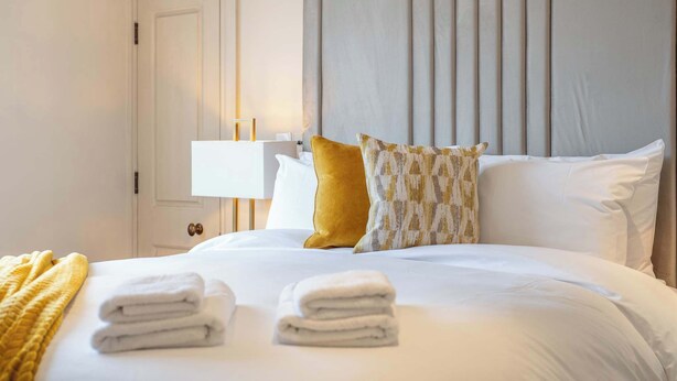 A hotel room with a neatly made bed, a bedside lamp, and a door.