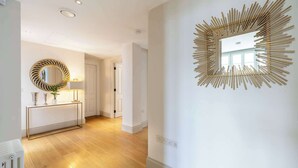 A hallway with a wooden floor, a round mirror with a geometric frame, and a wall-mounted sunburst mirror.