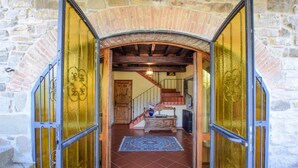 A stone building entrance with a wooden staircase leading to a room with a tiled floor and a blue rug. - Gorgeous home in Bibbiena (Bibbiena)