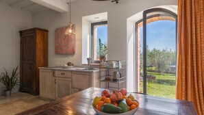 A kitchen with wooden cabinets, a large wooden table, a fruit bowl, and a view of a garden through a glass door. - Nice apartment for 2 guests with pool, WIFI and terrace, close to San Gimignano (Il Piano)