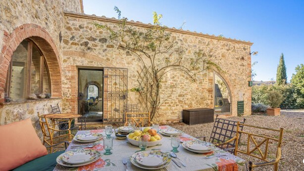 An outdoor dining area with a stone building, a table set with plates, glasses, and fruits, and wicker chairs. - Nice apartment for 2 guests with pool, WIFI and terrace, close to San Gimignano (Il Piano)