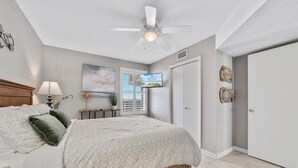Une chambre à coucher avec un lit, un ventilateur de plafond, une télévision, une fenêtre et une porte.