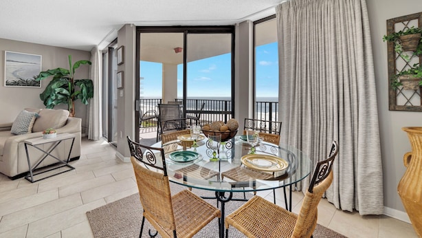 Un coin repas avec une table en verre, des chaises en osier et une vue sur l’extérieur.