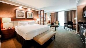 A hotel room with a large bed, a desk, a chair, a TV, and a window with curtains.
