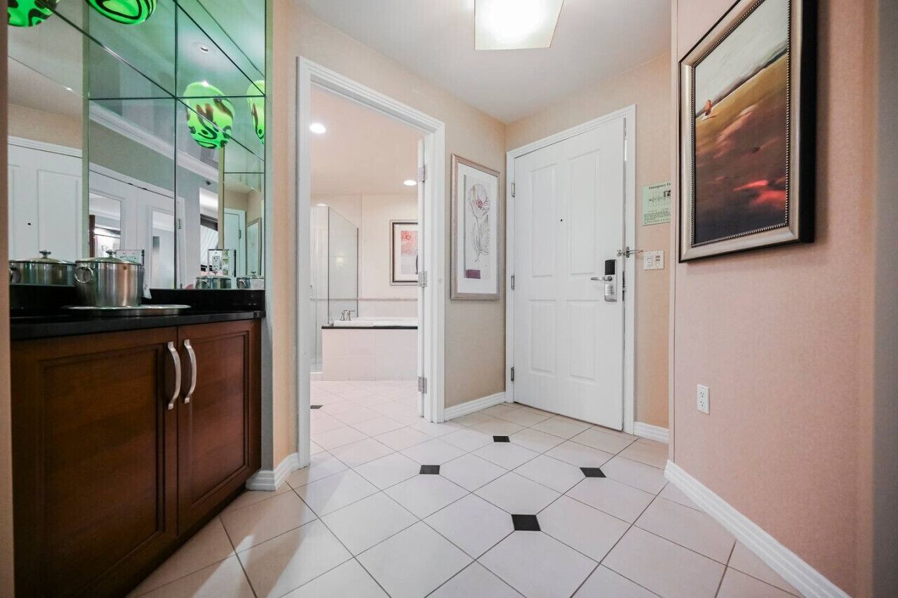 A hallway with a kitchen area, white tiled flooring, and a framed picture on the wall.