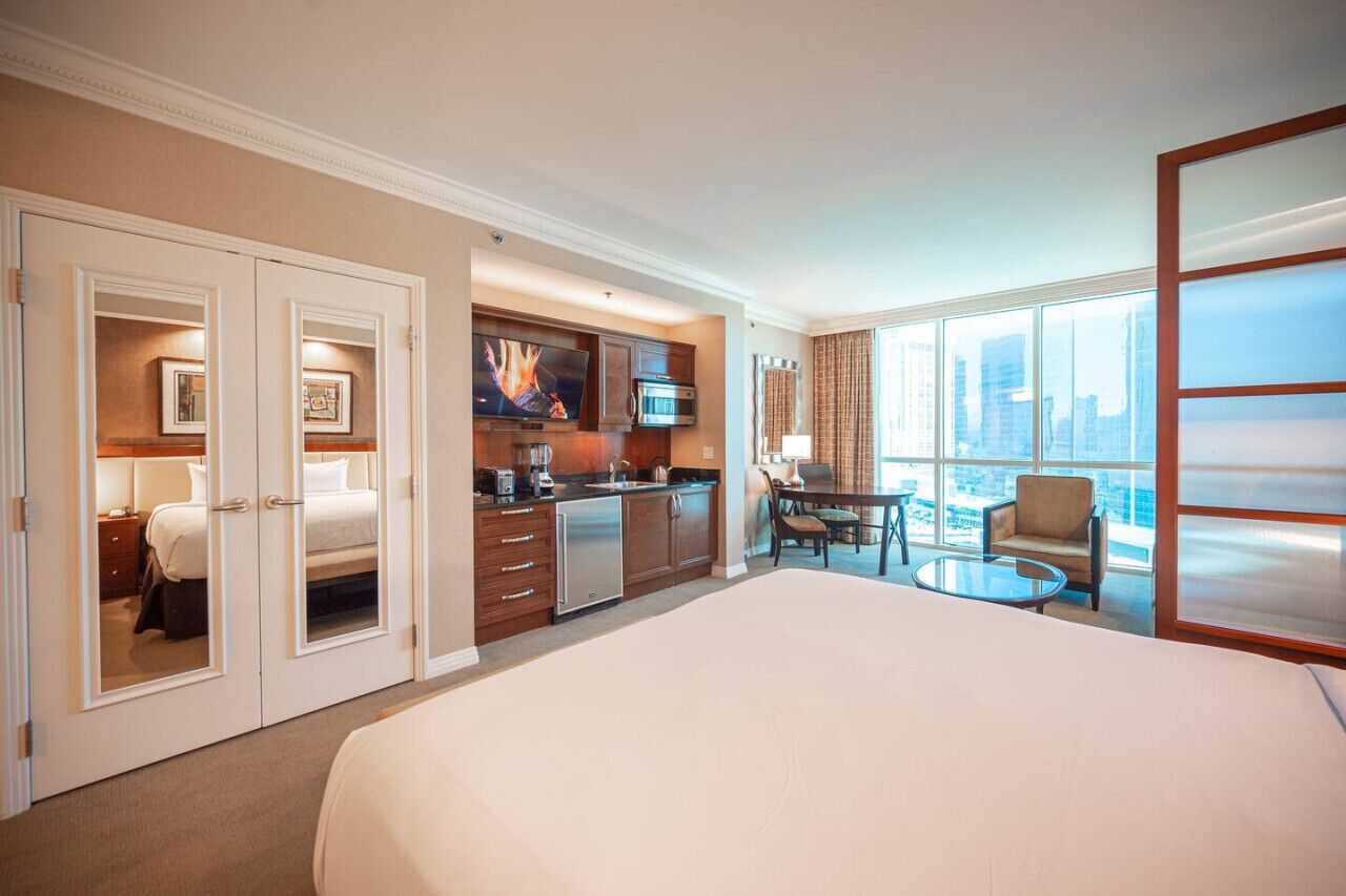 Een hotelkamer met een groot bed, een kitchenette, een eethoek en uitzicht op de stad.