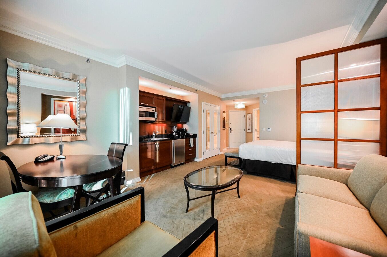 Een hotelkamer met een eettafel, een bank, een bed, een televisie en een keukenhoek.