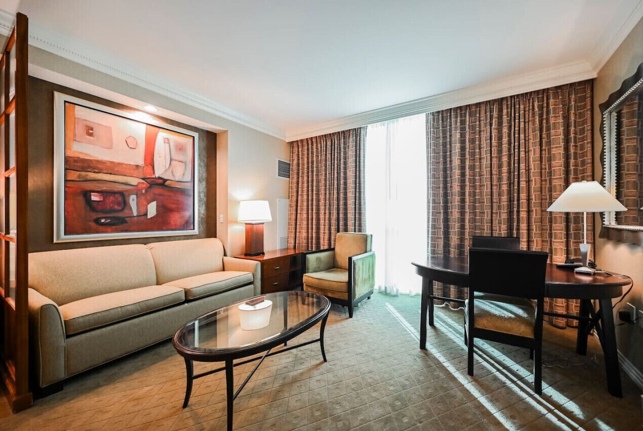 Een hotelkamer met een bank, een tafeltje, een stoel, een lamp en een schilderij aan de muur.