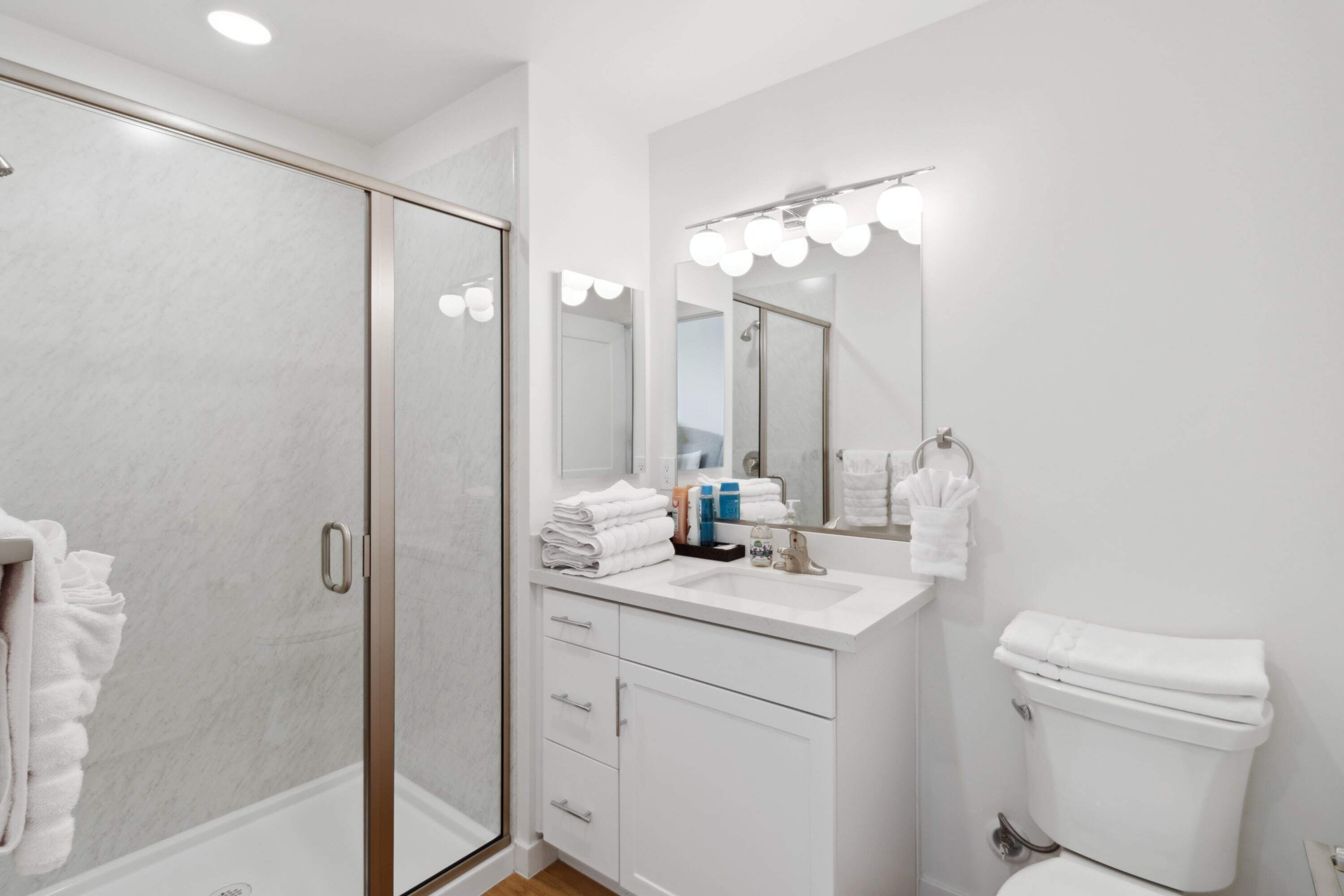 A modern bathroom with a glass shower enclosure, a vanity with a sink and mirror, and a toilet.