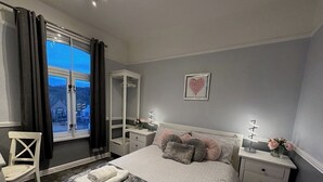 A bedroom with a bed, bedside tables, a chair, a window with curtains, and a heart-shaped decoration on the wall. - Stunning spacious one bedroom apartment in courtyard location, central to town (Belper)