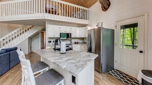Una cocina con una isla de mármol, armarios blancos, un refrigerador de acero inoxidable y un ventilador de techo.