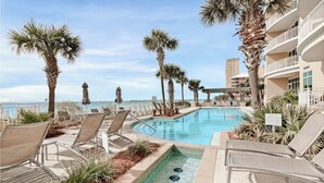 A pool area with lounge chairs and palm trees, overlooking a body of water.