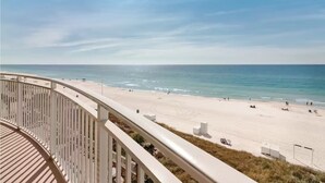 A beach view from a balcony with a railing, sandy beach, and ocean.
