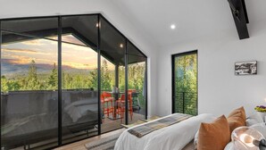 Un dormitorio moderno con una cama grande, un muro de cristal y vistas a un área boscosa.
