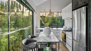 Una cocina moderna con ventanas amplias, un comedor con mesa y sillas, y vistas a zonas verdes al exterior.