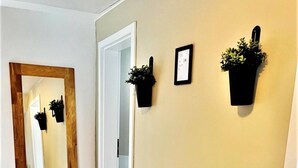 Ein Flur mit einem spiegelnden Holzboden, zwei Wandgehänge mit Pflanzen und einer Tür zu einem weiteren Raum.
