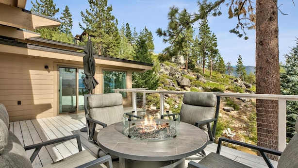 A deck with a round table and chairs, a fire pit, and a view of a mountainous landscape. - Luxury Mountain retreat with Hot tub (Zephyr Cove)