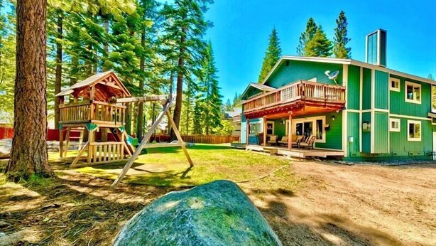 Eine zweistöckige Holzhütte mit einer Holzterrasse und einem großen Felsen im Vordergrund.