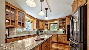 Eine Küche mit Granit Arbeitsplatten, Holzschränken, einem Edelstahlkühlschrank und Pendelleuchten.